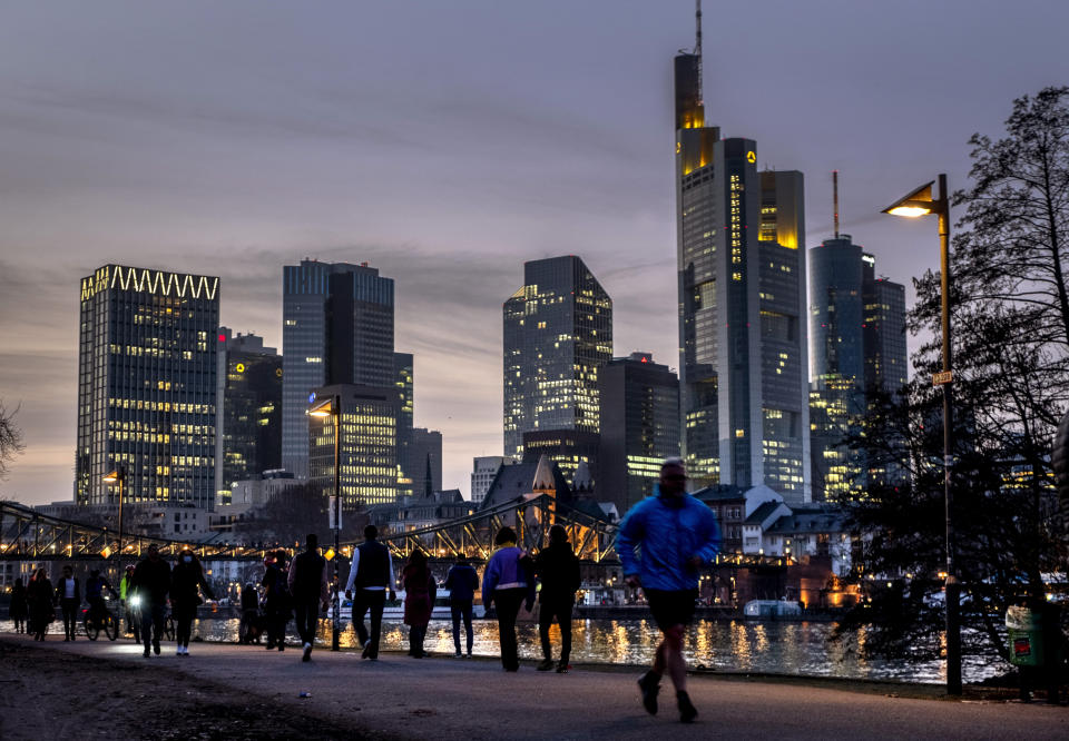 People stroll along the river Main with the buildings of the banking district in background in Frankfurt, Germany, Thursday, Feb. 25, 2021. (AP Photo/Michael Probst)