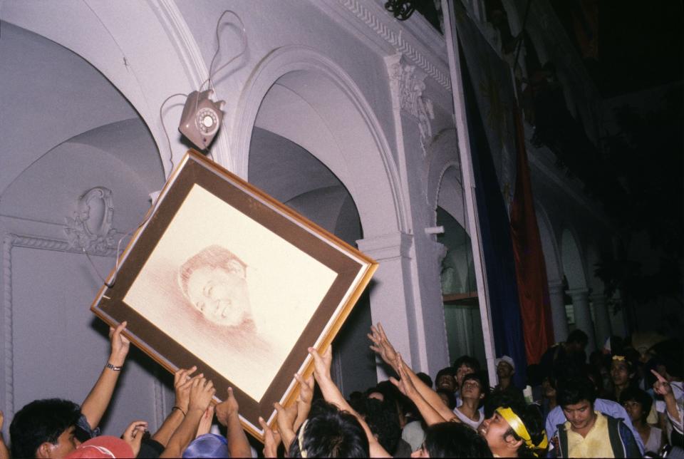 A telephone hurtles through the air to join a portrait painting of President Ferdinand Marcos that is being lowered from the balcony of Malacanang Palace by protestors llooting the Presidential Palace, Manila, 25th February 1986. The mass demonstrations, which came to be known as the People Power Revolution, or EDSA Revolution, toppled Marcos after four days.