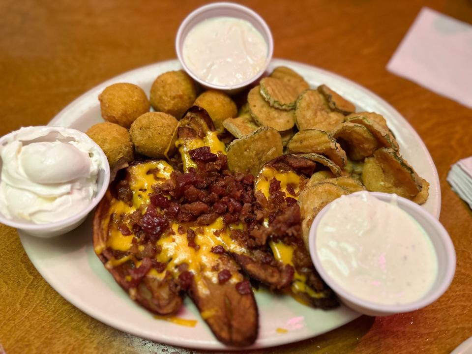 Potato skins topped with cheese and bacon bits next to fired pickles with three dipping sauces