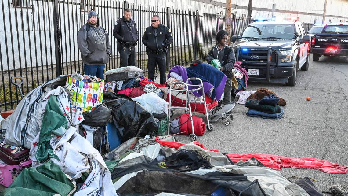 Fresno police officers stand near a pair of homeless people with their belongings pulled to the side of the street as Fresno’s Homeless Assistance Response Team (HART) begins a homeless camp cleanup operation behind several shelters on Parkway Drive in Fresno on Wednesday, Feb. 1, 2023