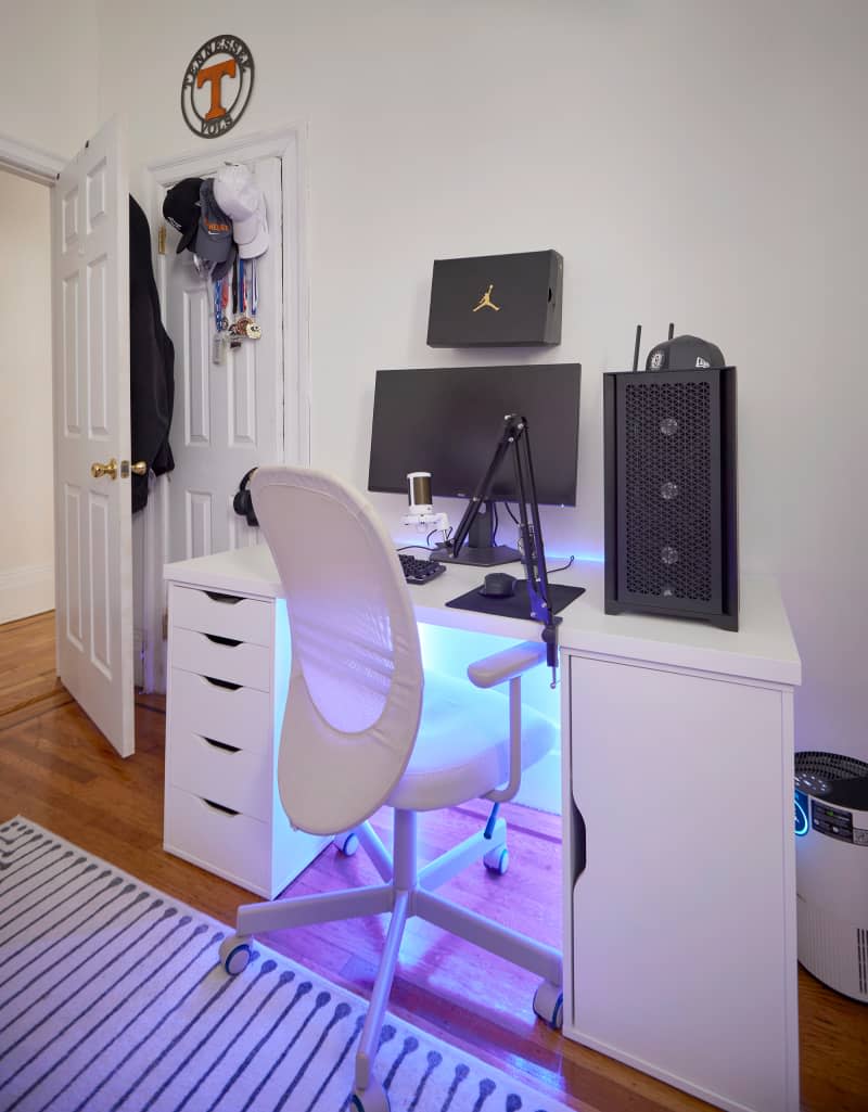 Computer on white under-lit desk and chair in white bedroom.