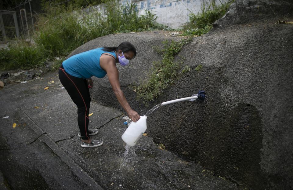 FILE - In this April 22, 2020, file photo, a woman wearing a face mask as a precaution from the coronavirus collects water on the side of the road to take home in Caracas, Venezuela. For people around the world who are affected by war and poverty, the simple act of washing hands is a luxury. (AP Photo/Ariana Cubillos)