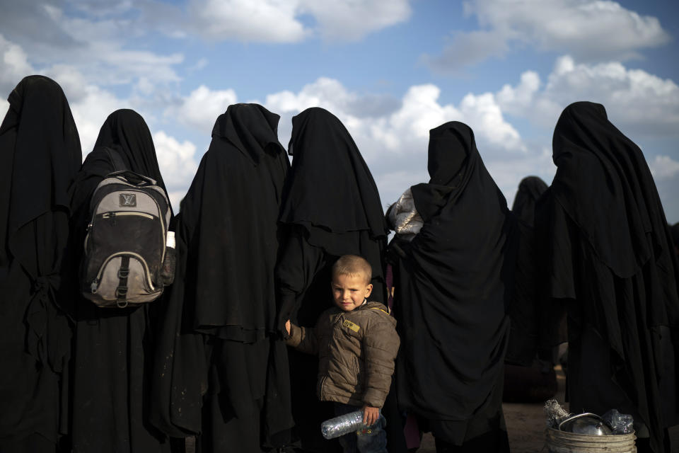 A boy holds her mother's hand as they wait to be screened after being evacuated out of the last territory held by Islamic State militants, near Baghouz, eastern Syria, Friday, Feb. 22, 2019. (AP Photo/Felipe Dana)