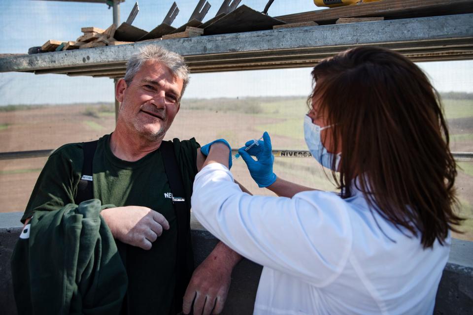 Casey Villhauer, owner and pharmacist at VaxiTaxi, gives a dose of the Pfizer COVID-19 vaccine to construction worker Safet Tabakovi on Sunday atop a 130-foot-tall minaret at the Islamic and Cultural Center Bosniak in Granger, Iowa.