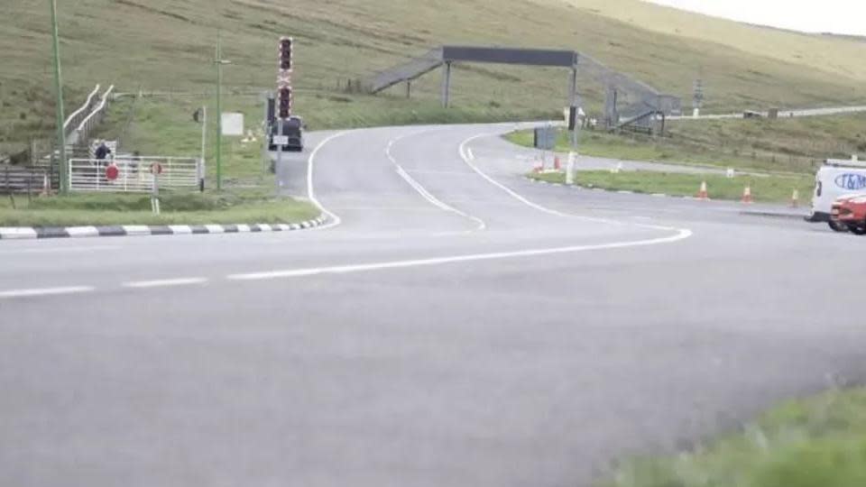 A road snaking up a hill with a metal footbridge over the carriageway