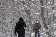 People wearing a face mask to protect against coronavirus walk through a snow covered street in Belgrade, Serbia, Sunday, Jan. 17, 2021. Meteorologists predict sub zero temperatures in Serbia throughout the coming week. (AP Photo/Darko Vojinovic)