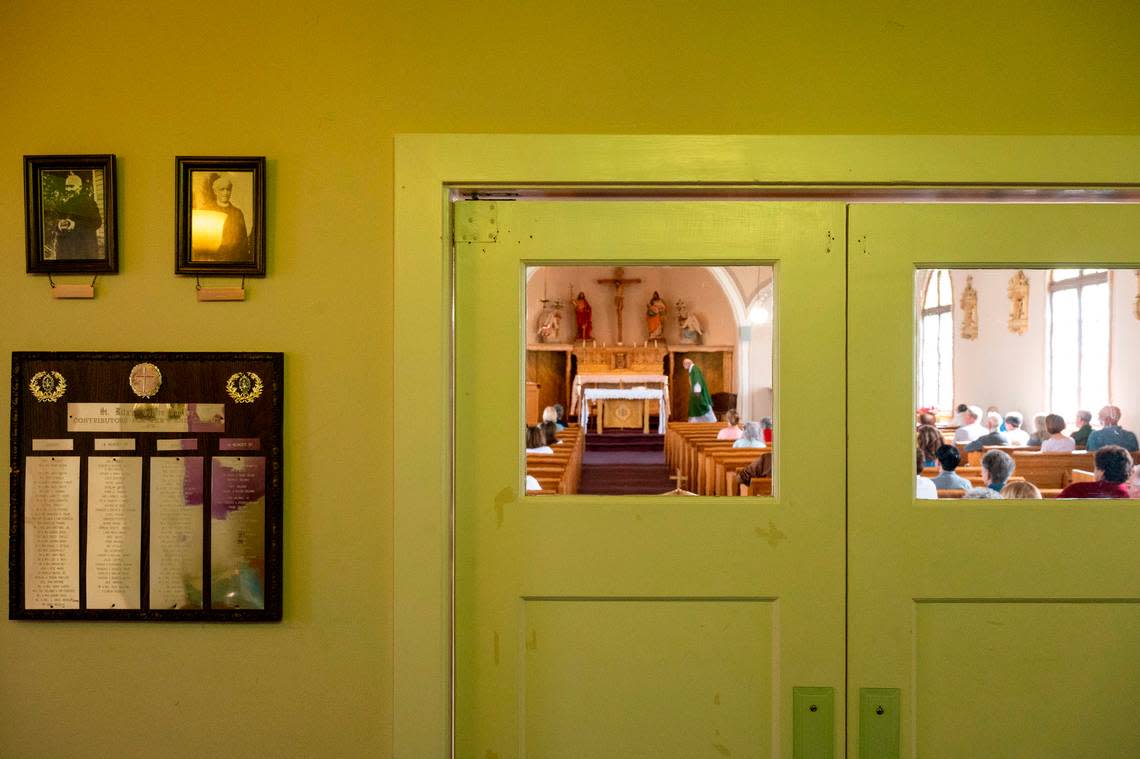 Pictures of former priests and plaques of members of the parish hang on the wall of the entryway as Father Ron Knudsen walks toward the altar during the final Mass at St. Rita of Cascia on Wednesday, June 8, 2022, in the Hilltop neighborhood of Tacoma.