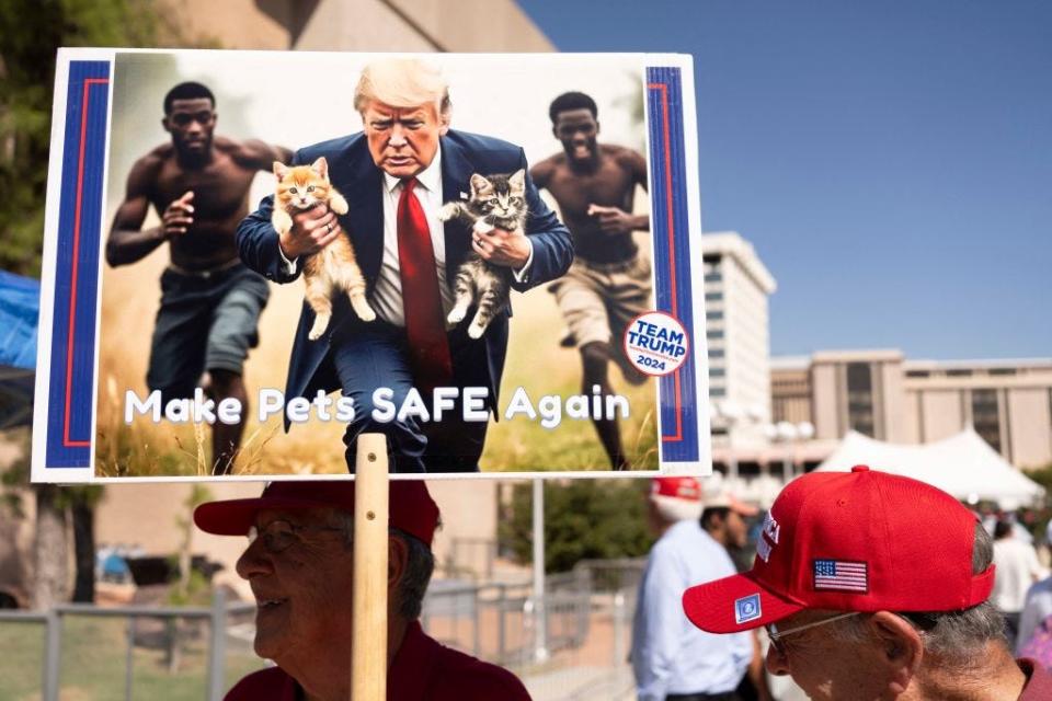 A man carries an AI-generated image of former President Donald Trump taking cats away from Haitian immigrants, a reference to falsehoods being spread about Springfield, Ohio.