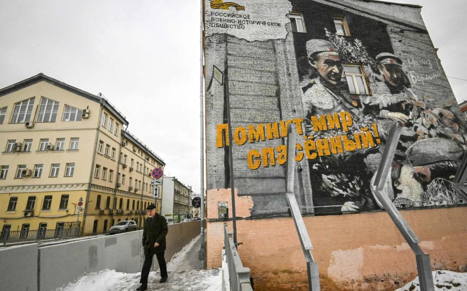 A pedestrian walks past a building decorated with a mural depicting a photograph of World War Two times with the slogan reading "And the saved world remembers!" in Moscow - YURI KADOBNOV/AFP