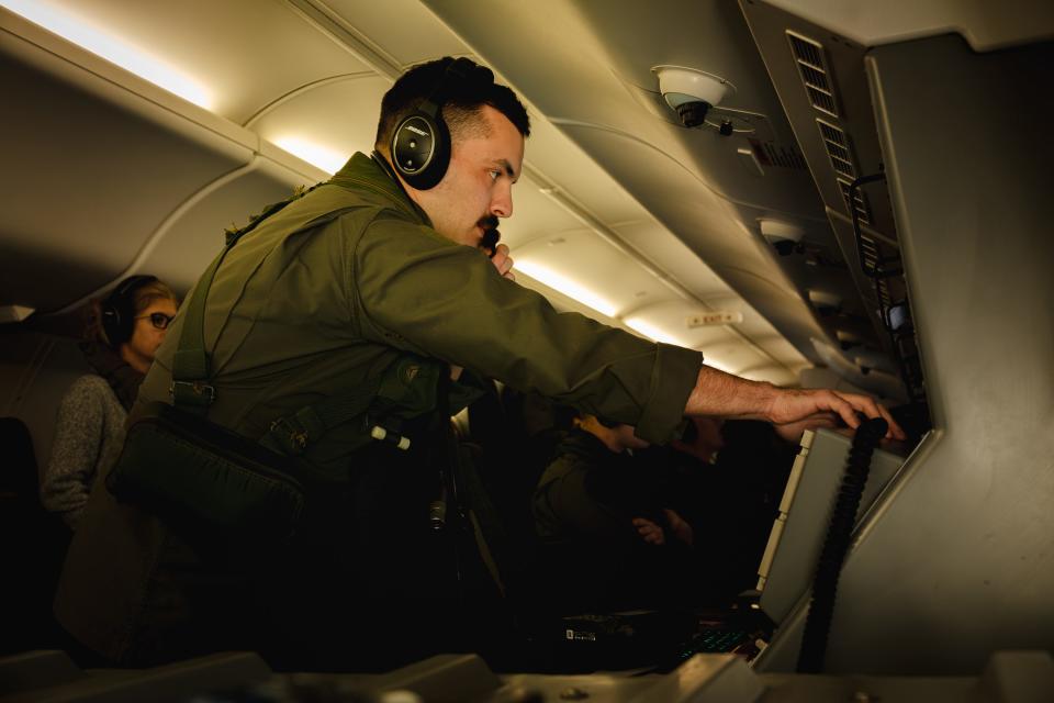 A man talks on a radio and stands in front of a console inside a plane.