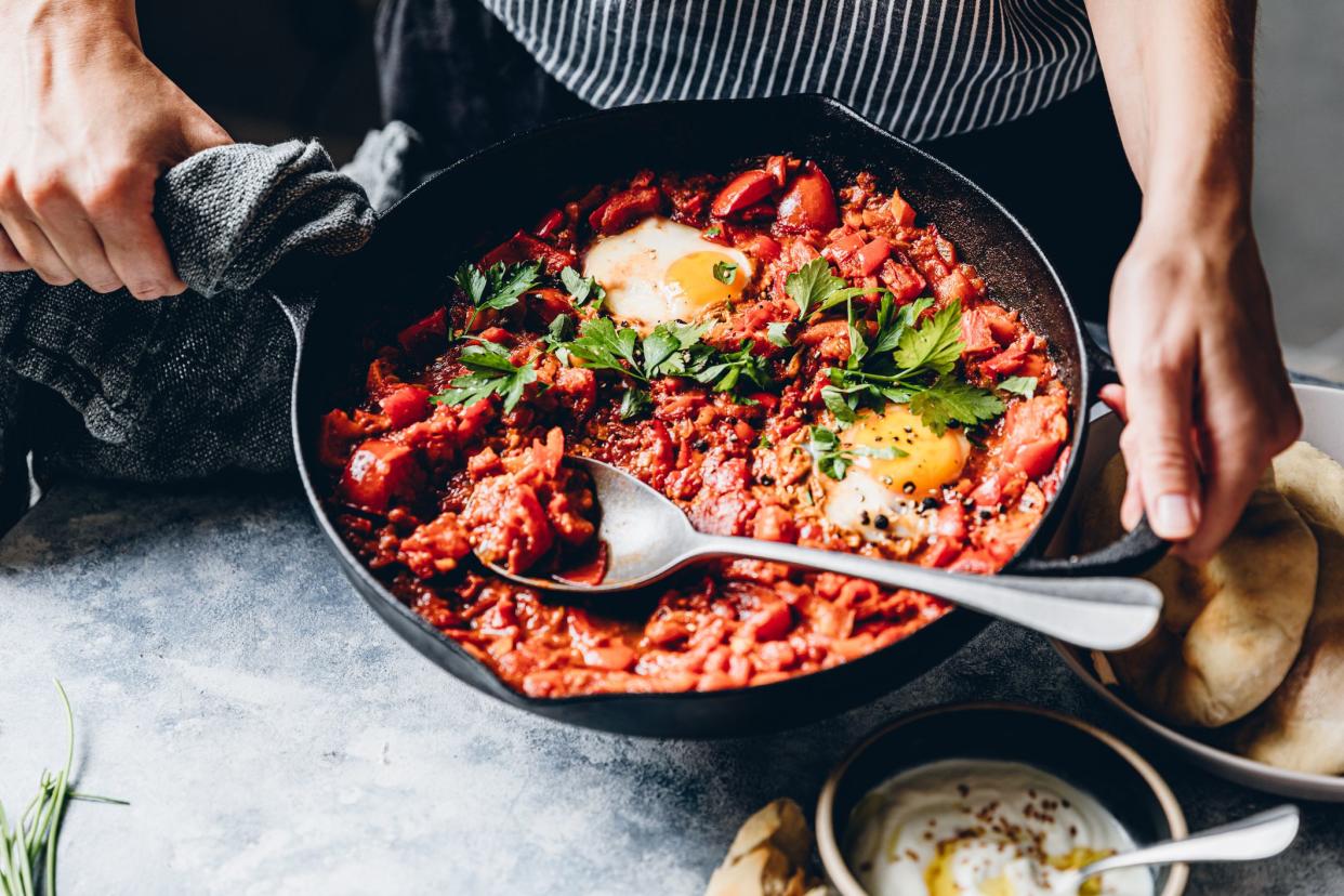 Woman preparing shakshuka with poached egg in kitchen. Female chef preparing a vegan dish.