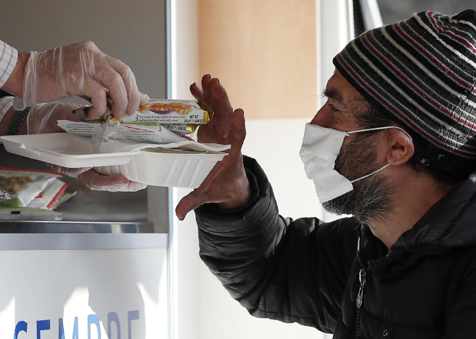 A volunteer serves food and drinks to a homeless man in Milan, Italy, Saturday, Nov. 7, 2020. As the Italian government placed four regions, including hard-hit Lombardy, into effective lockdown for two weeks because infections and hospital saturation levels were rising fast, canteens and shelters for homeless people had to be shut down, leaving them with nowhere to get a meal. (AP Photo/Antonio Calanni)