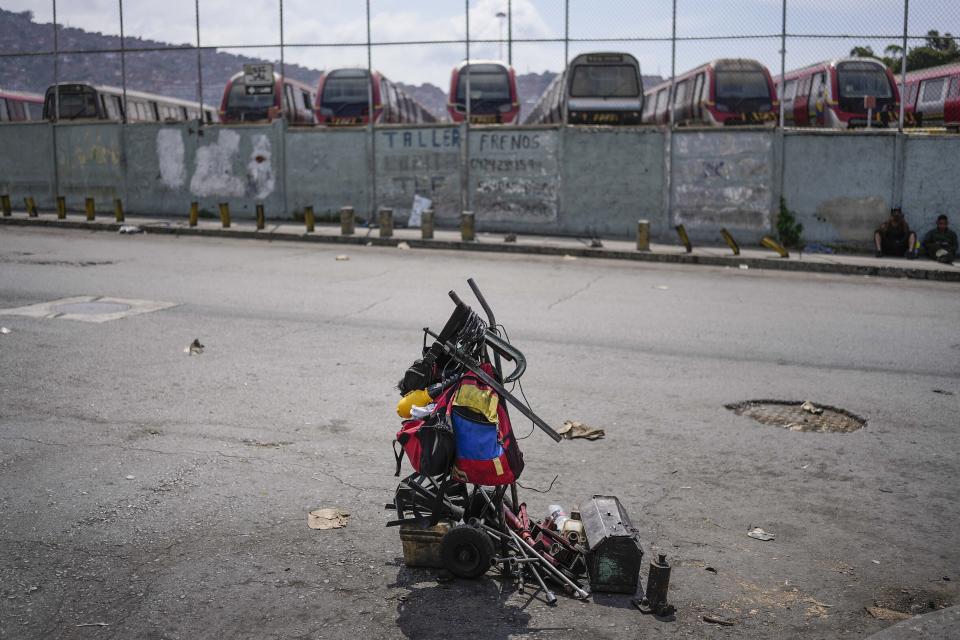 A backpack with the colors of the Venezuelan flag hangs on a wheelbarrow with tools near where cars are repaired on the street of the Catia neighborhood of Caracas, Venezuela, Tuesday, April 19, 2022. Mechanics are increasingly busy as they try to coax a little more life out of aging vehicles in a country whose new car market collapsed and where few can afford to trade up for a better used one. (AP Photo/Matias Delacroix)