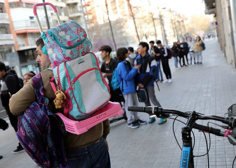 Father carries the backpack of his daughter as he waits for her at entrance of a school in Barcelona