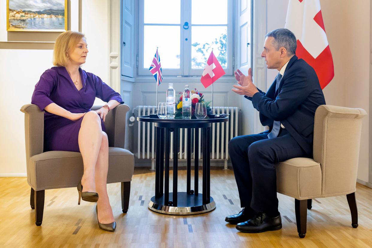 Elizabeth Truss and President Ignazio Cassis, each seated in armchairs, hold a conversation with their national flags placed on the table between them.. 