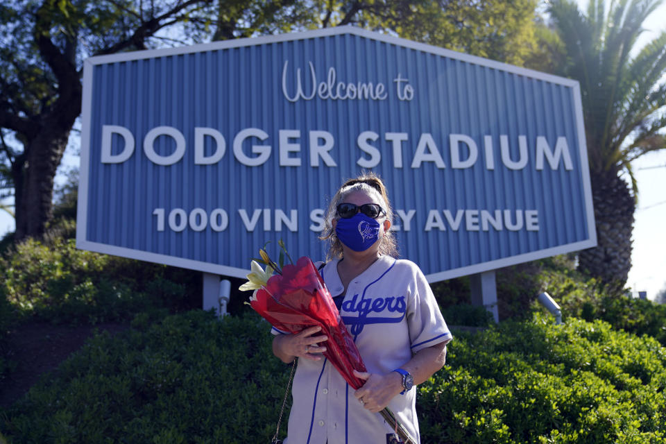 Los Angeles Dodgers fan Michelle Santisteban carries flowers to place in front of a stadium sign outside of Dodger Stadium Friday, Jan. 8, 2021, in Los Angeles. Tommy Lasorda, the fiery Hall of Fame manager who guided the Los Angeles Dodgers to two World Series titles and later became an ambassador for the sport he loved during his 71 years with the franchise, has died. He was 93. (AP Photo/Marcio Jose Sanchez)