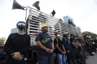 Security staff stand in front of a truck used as a stage during a rally outside the Siam Commercial Bank,a publicly-held company in which the Thai king is the biggest shareholder,Wednesday, Nov. 25, 2020, in Bangkok Thailand. Thai authorities have escalated their legal battle against the students leading pro-democracy protests, charging 12 of them with violating a harsh law against defaming the monarchy. (AP Photo/Sakchai Lalit)