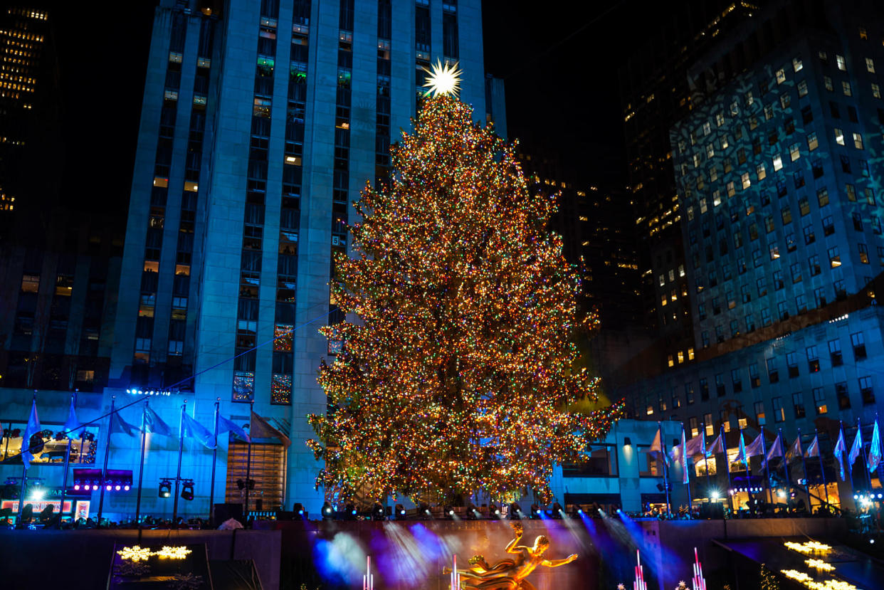 A giant christmas tree stands above a gold statue and ice skating rink surrounded by tall new york city buildings. (Lokman Vural Elibol / Anadolu Agency via Getty Images)