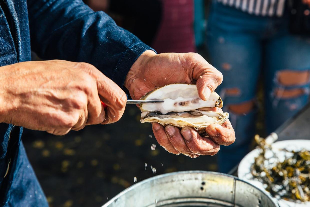 Close up of a man opening oyster shell with a knife - stock photo