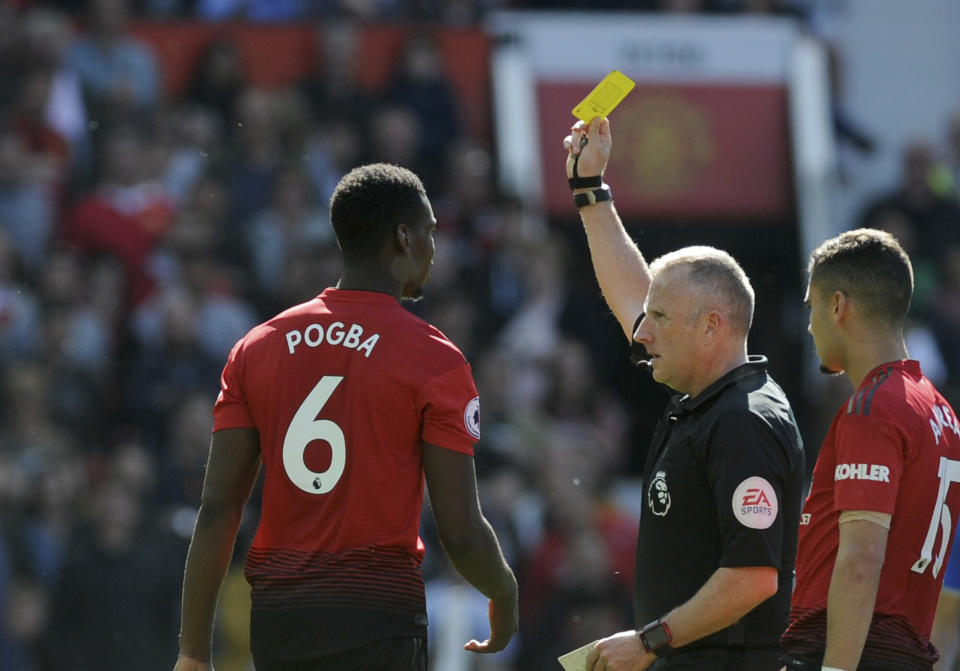 Referee Jonathan Moss, center, shows a yellow card to Manchester United's Paul Pogba, left, during the English Premier League soccer match between Manchester United and Cardiff City at Old Trafford in Manchester, England, Sunday, May 12, 2019. (AP Photo/Rui Vieira)