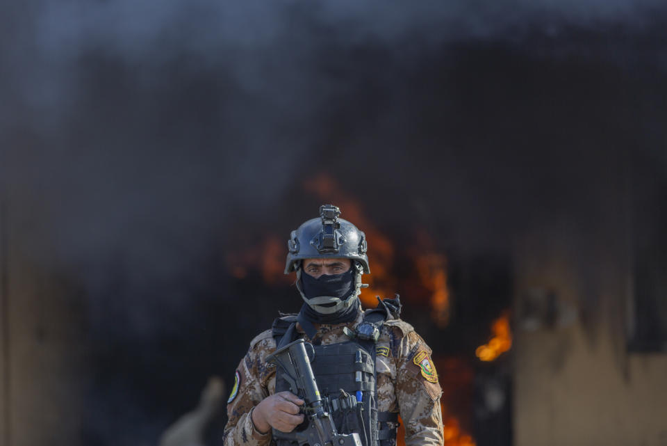 An Iraqi soldier stands guard in front of smoke rising from a fire set by pro-Iranian militiamen and their supporters in the U.S. embassy compound, Baghdad, Iraq, Wednesday, Jan. 1, 2020. U.S. troops fired tear gas on Wednesday as hundreds of Iran-backed militiamen and other protesters gathered outside the American Embassy in Baghdad for a second day and set fire to the roof of a reception area inside the compound. (AP Photo/Nasser Nasser)