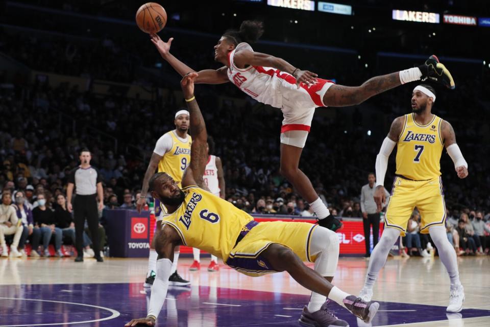 A basketball player jumps in the air with the ball as an opponent player falls down.