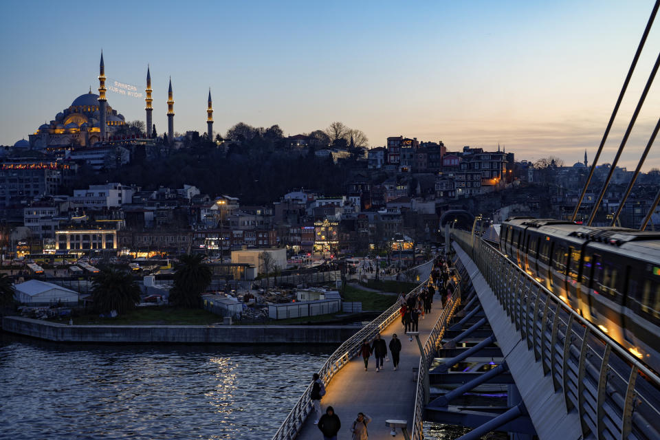 Backdropped with Suleymaniye mosque, top left, pedestrians walk along Halic bridge metro station on the first day of the Muslim holy fasting month of Ramadan in Istanbul, Turkey, Sunday, March 10, 2024. (AP Photo/Emrah Gurel)