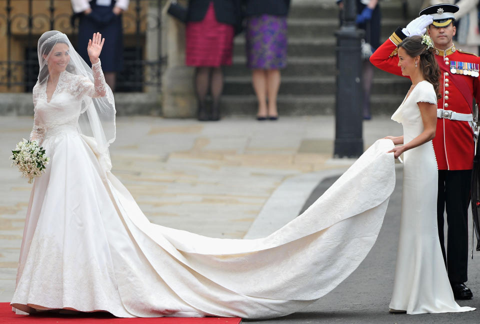 Kate waves to the crowds as her sister and maid of honor, Pippa Middleton, holds her dress before walking in to Westminster Abbey. (Photo: Pascal Le Segretain via Getty Images)