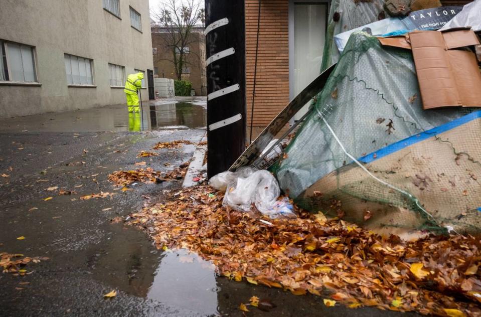 A city of Sacramento worker clears a drain in Government Alley at 10th Street near an encampment as a weather system moving through the region brings rain and gusting winds Saturday, Dec. 10, 2022.