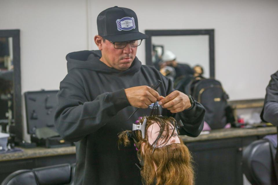 An East to West Academy student practices how to perm hair on a mannequin's head.