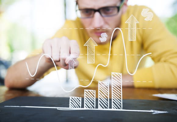 A man points at a drawing of an ascending bar chart floating in front of him.