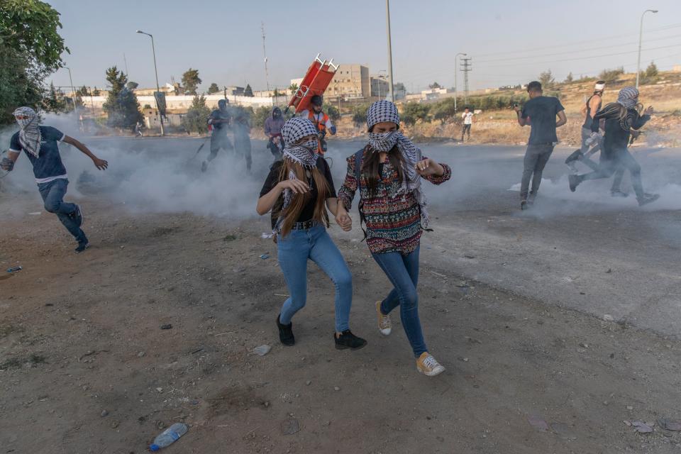 Palestinian protesters run to avoid teargas during clashes with Israeli soldiers at the northern entrance of the West Bank city of RamallahAP