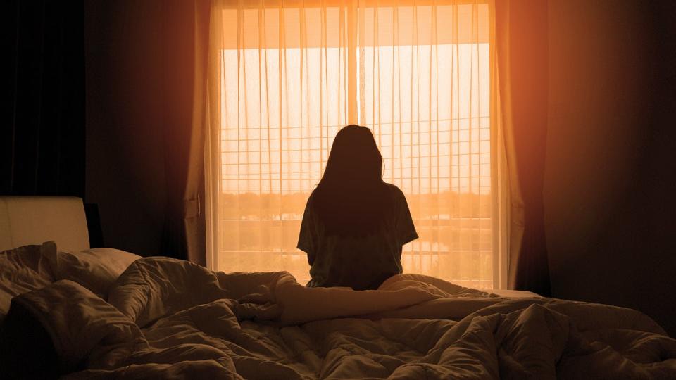 Woman sits on the end of a bed.