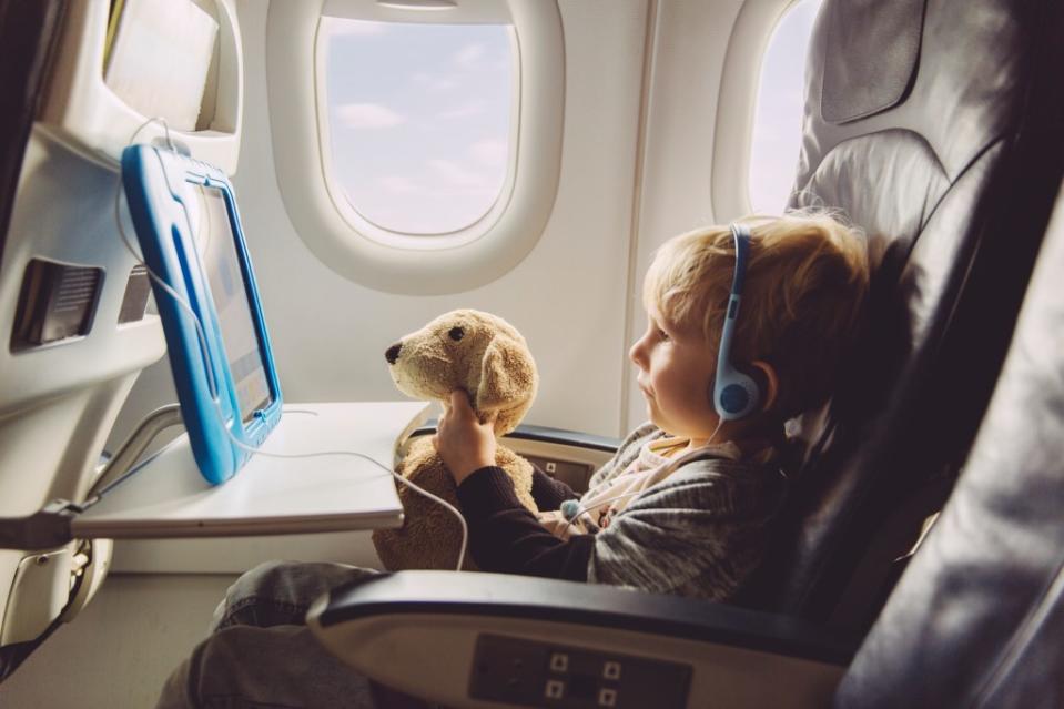 Little boy watching something on a digital tablet with his plush dog while flying on an airplane via Getty Images