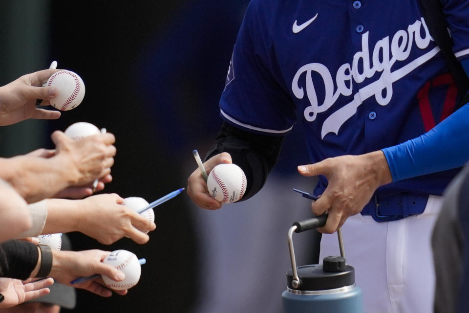 Los Angeles Dodgers designated hitter Shohei Ohtani signs autographs for fans before a spring training baseball game against the Chicago White Sox in Phoenix, Tuesday, Feb. 27, 2024. (AP Photo/Ashley Landis)