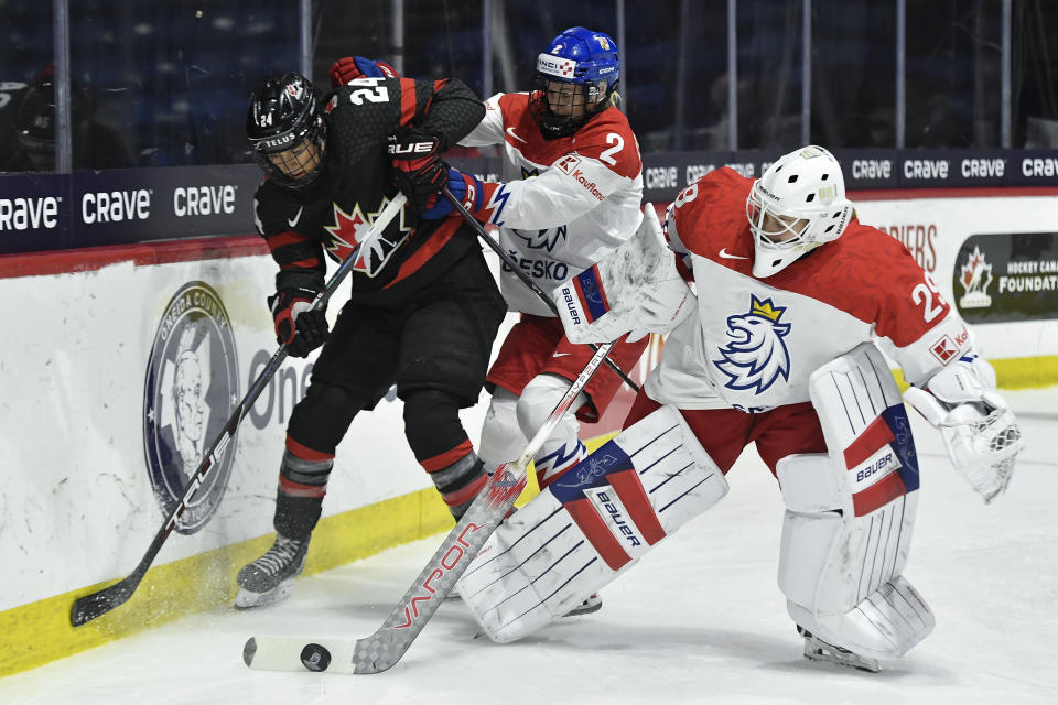 Czechia goalie Klara Peslarova, right, clears the puck as defenseman Aneta Tejralova, center, defends against Canada forward Natalie Spooner during the first period of a semifinal at the women's world hockey championships in Utica, N.Y., Saturday, April 13, 2024. (AP Photo/Adrian Kraus)