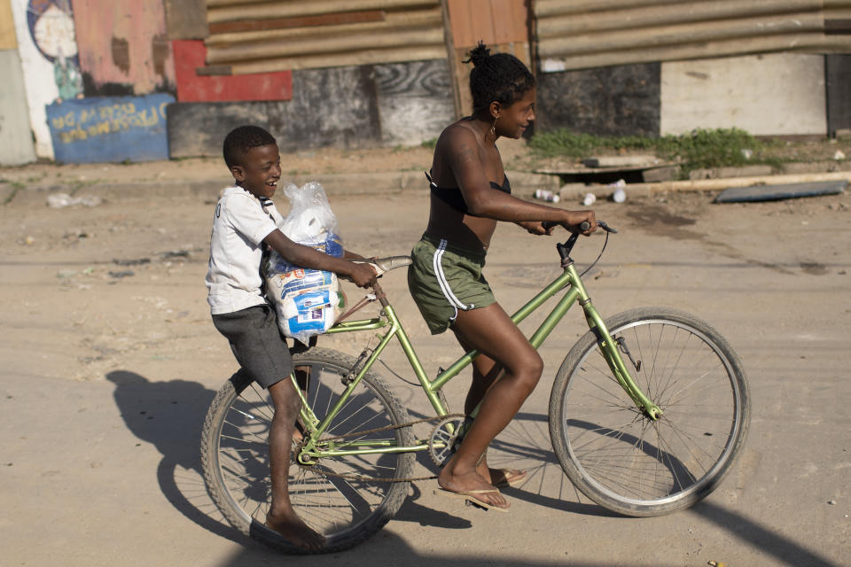 Youths carry home food donated from the Covid Without Hunger organization in the Jardim Gramacho slum of Rio de Janeiro, Brazil, Saturday, May 22, 2021. Poverty — defined as households living on less than one minimum wage — spiked in the first quarter of 2021 to its highest level in at least nine years, after plunging last year, according to Marcelo Neri, director of the Getulio Vargas Foundation's social policy center.(AP Photo/Silvia Izquierdo)