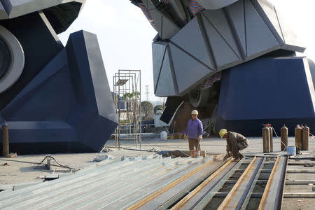 Construction workers smooth out steel rods in front of the feet of a giant robot statue at the Oriental Science Fiction Valley theme park in Guiyang, Guizhou province, China November 16, 2017. REUTERS/Joseph Campbell/Files