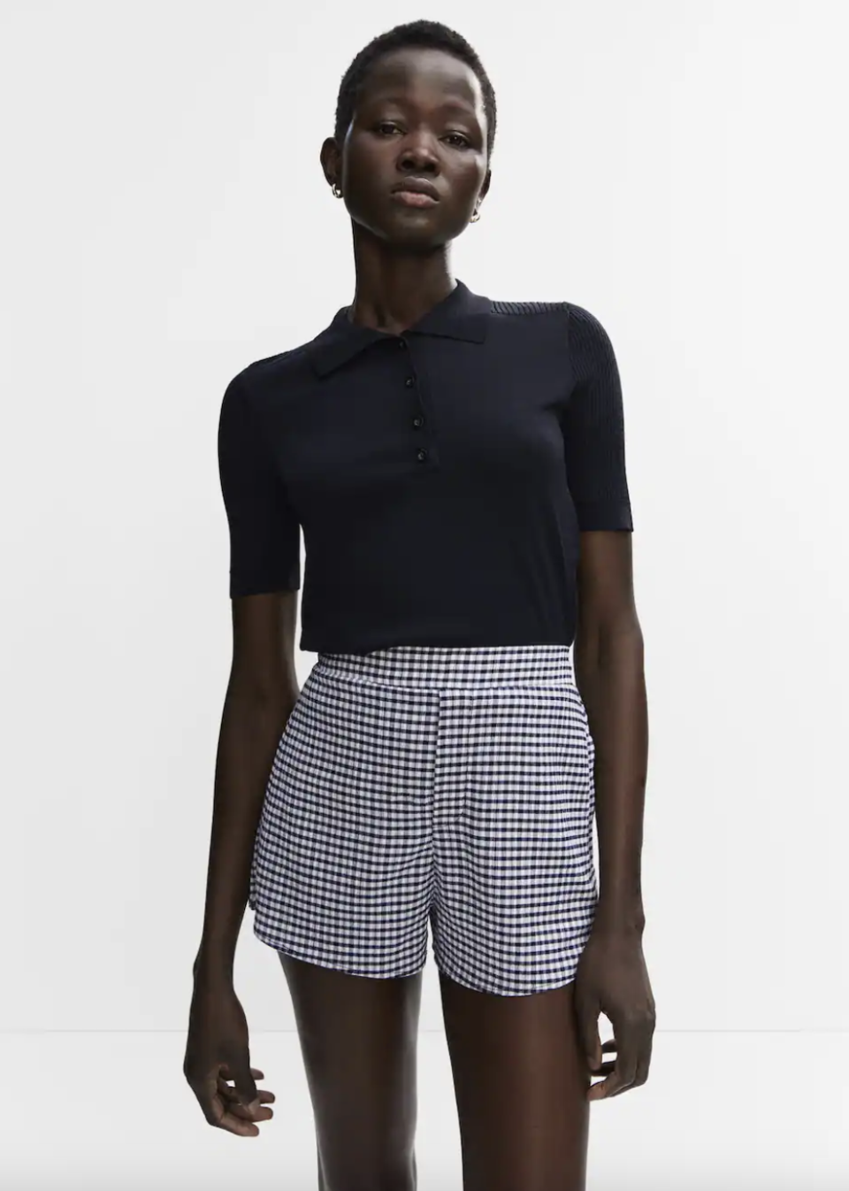 model wearing dark navy blue shirt and blue and white Gingham shorts (Photo via Mango)