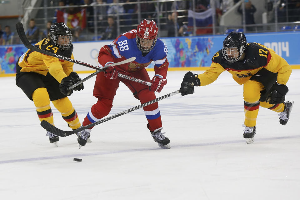 Yekaterina Smolina of Russia is sandwiched between Lisa Christine Schuster, left and Sara Seiler of Germany as they battle for the puck during the first period of the 2014 Winter Olympics women's ice hockey game at Shayba Arena, Sunday, Feb. 9, 2014, in Sochi, Russia. (AP Photo/Petr David Josek)