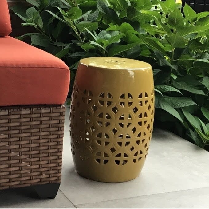 Ceramic garden stool with cut-out design next to a wicker sofa with red cushions, set against green plants. Perfect for outdoor decor