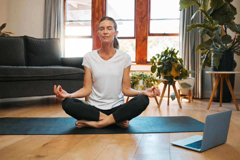 Woman meditating in her living room using a laptop for guided meditation.