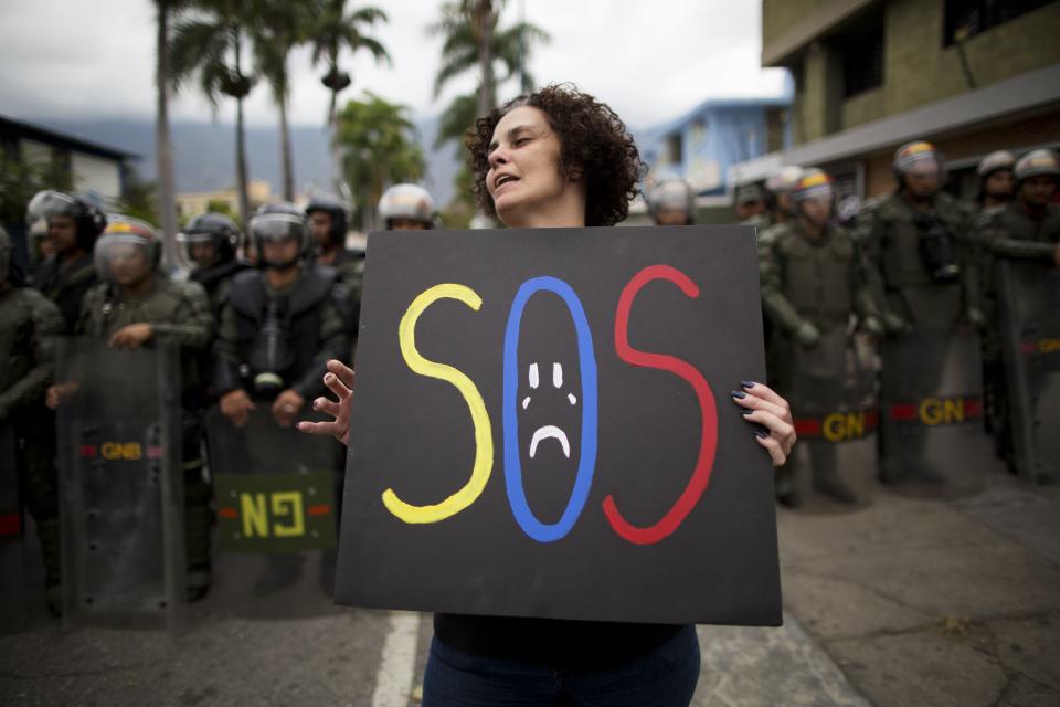 A demonstrator holds a homemade poster in front of a cordon of National Bolivarian National Guard during a protest near the Cuban embassy in Caracas, Venezuela, Tuesday, Feb. 25, 2014. Opponents of President Nicolas Maduro marched to the Cuban Embassy to protest what they consider the communist nation's interference in Venezuela's internal affairs. (AP Photo/Rodrigo Abd)