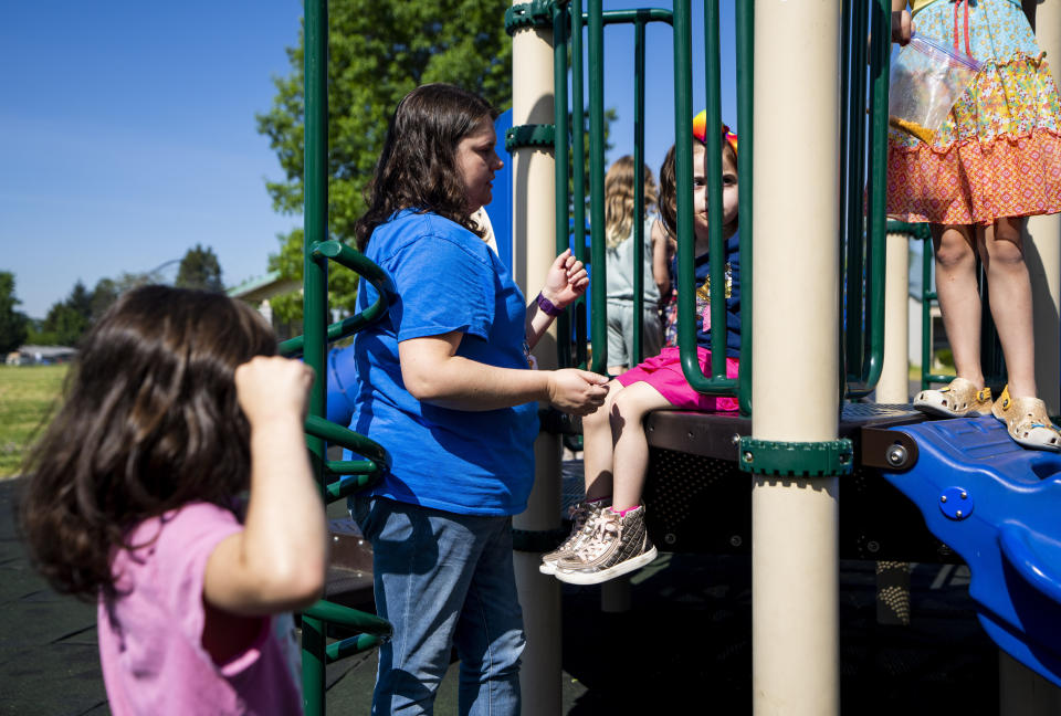 Vivien Henshall, a long-term substitute special education teacher, talks with Scarlett Rasmussen, 8, during recess at Parkside Elementary School Wednesday, May 17, 2023, in Grants Pass, Ore. Scarlett is nonverbal and uses an electronic device and online videos to communicate, but reads at her grade level. She was born with a genetic condition that causes her to have seizures and makes it hard for her to eat and digest food, requiring her to need a resident nurse at school. (AP Photo/Lindsey Wasson)