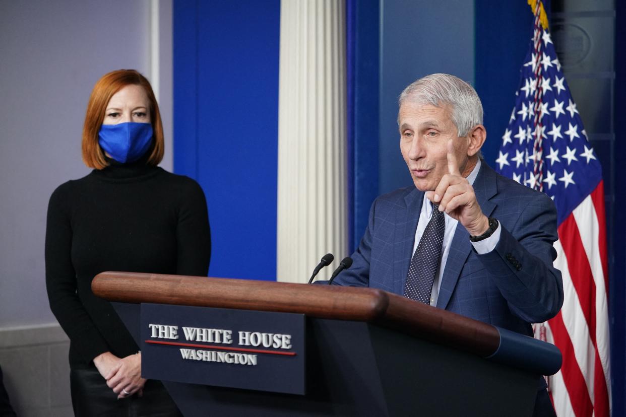 Dr. Anthony Fauci speaks at a podium while press secretary Jen Psaki listens during a daily briefing at the White House.