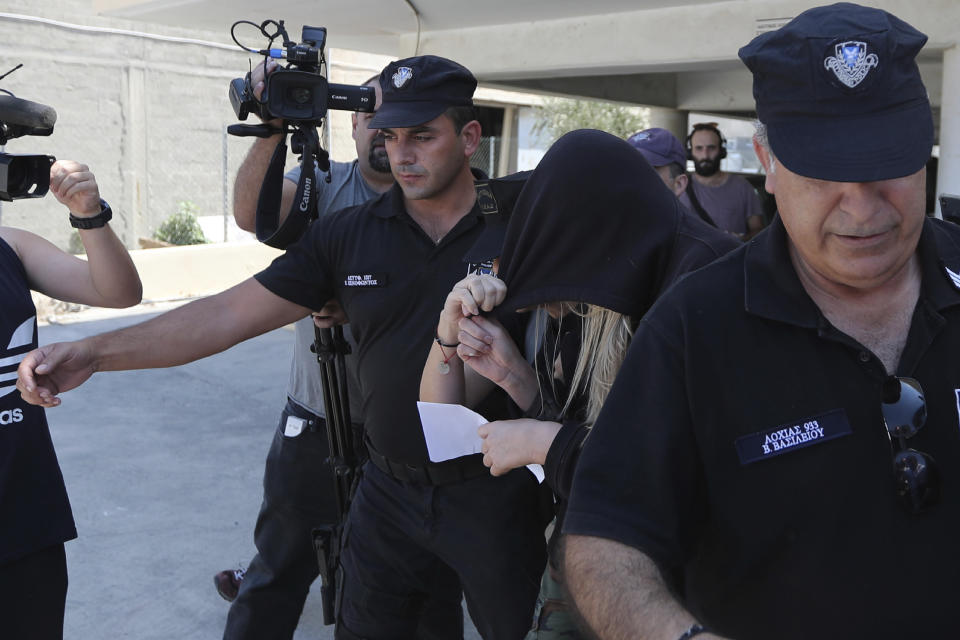 Elite police unit officers escort a 19-year old British woman, center with head covered, to Famagusta court in Paralimni, Cyprus, Tuesday, July 30, 2019. The British woman faces a public nuisance charge after she admitted that her accusation that 12 Israeli teens raped her at a popular resort town was untrue.(AP Photo/Petros Karadjias)