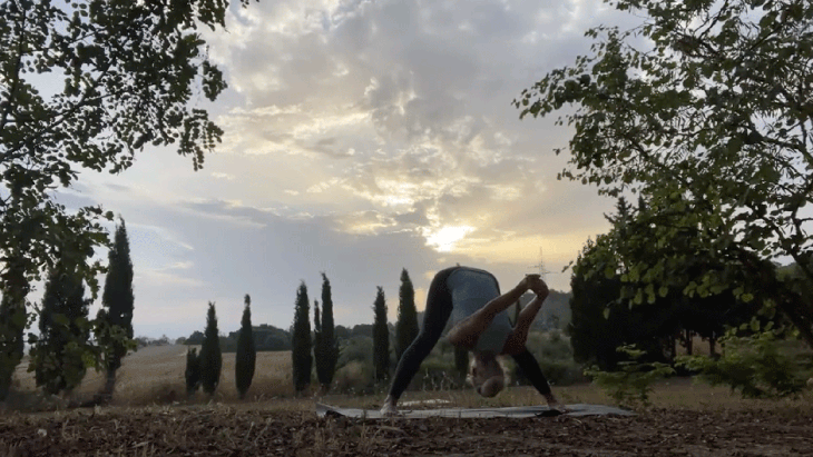 Woman standing on her yoga mat at sunrising stretching her hamstrings and shoulders