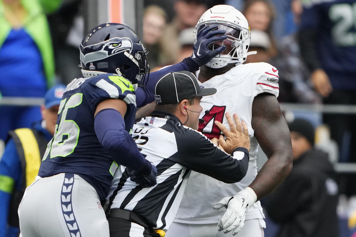 Seattle Seahawks linebacker Jordyn Brooks, left, pushes Arizona Cardinals offensive tackle D.J. Humphries, right, as down judge Brian Sakowski, center, tries to separate the two during the first half of an NFL football game Sunday, Oct. 22, 2023, in Seattle. Cardinals' Humphries was ejected from the game. (AP Photo/Lindsey Wasson)