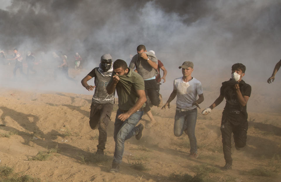 Palestinian protesters run for cover from teargas fired by Israeli troops during a protest at the Gaza Strip's border with Israel, Friday, Sept.28, 2018. (AP Photo/Khalil Hamra)