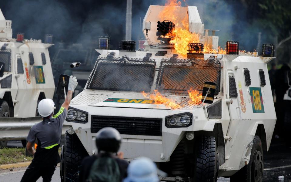 Demonstrators clash with a riot police armored car during a rally against Nicholas Maduro - Credit: Reuters